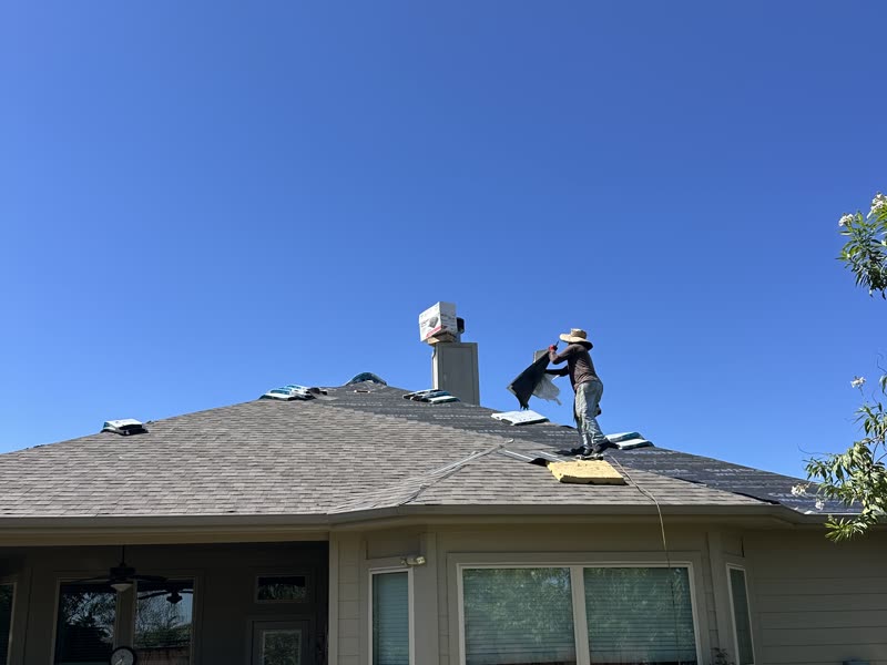 A Roof Boss ATX roofer laying underlayment across a hip roof during a replacement.